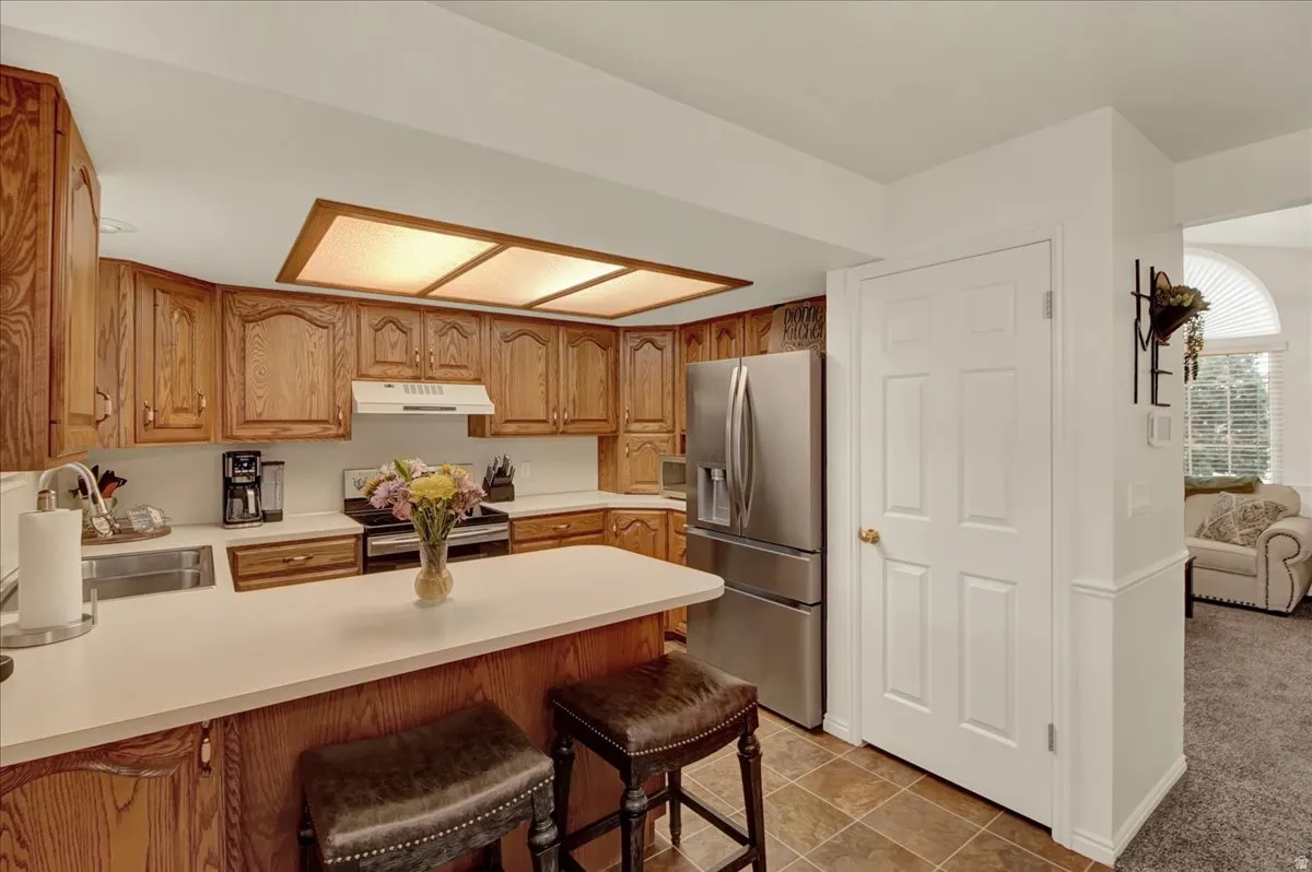 Warm wood cabinetry frames this kitchen, featuring stainless steel appliances, a spacious island with seating for two, recessed ceiling lighting, and tile flooring