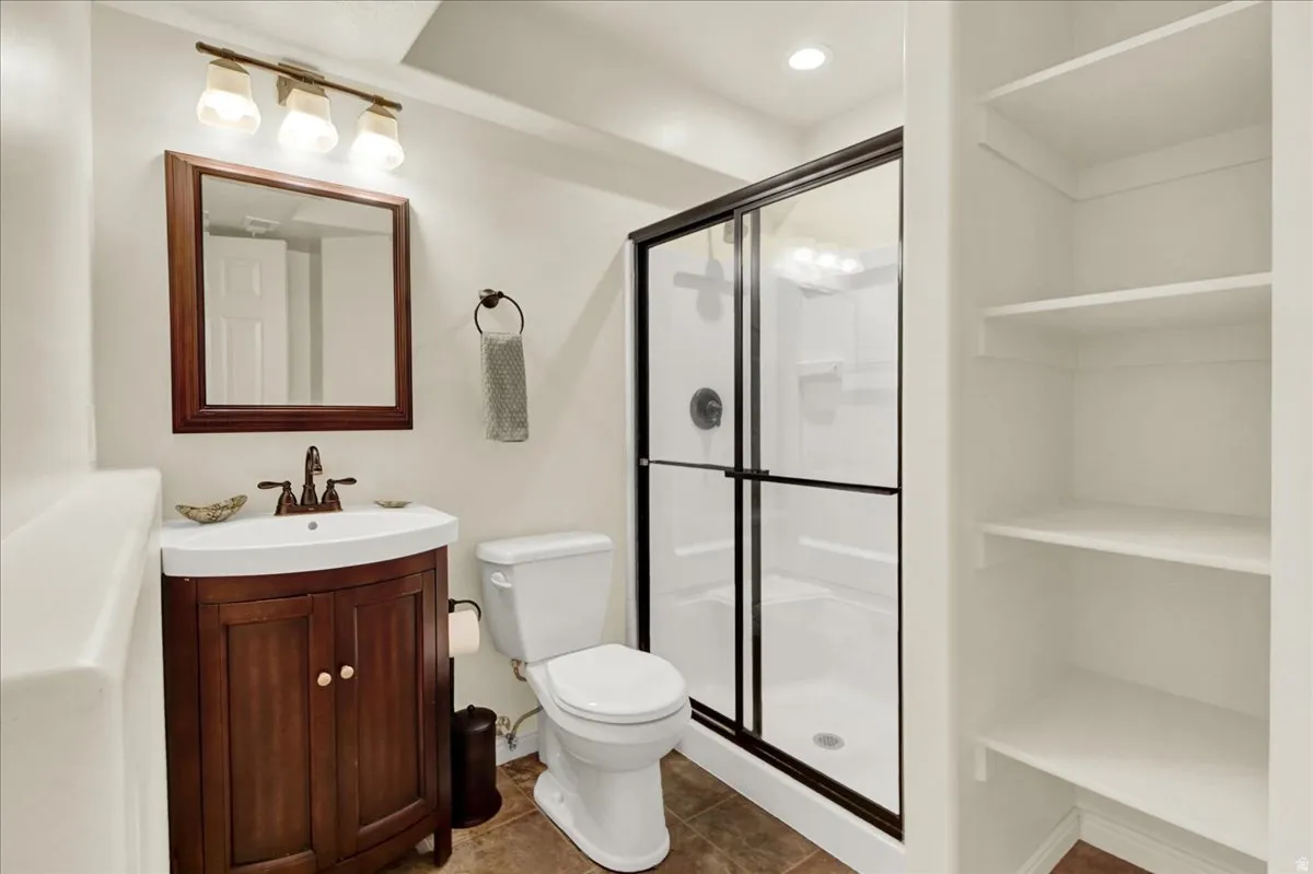 Spa-inspired bathroom featuring a wood-finish vanity with dual-handle faucet, white subway tile walls, recessed shelving, framed mirror with wood trim, and a frameless glass-enclosed shower with tile surround and chrome hardware