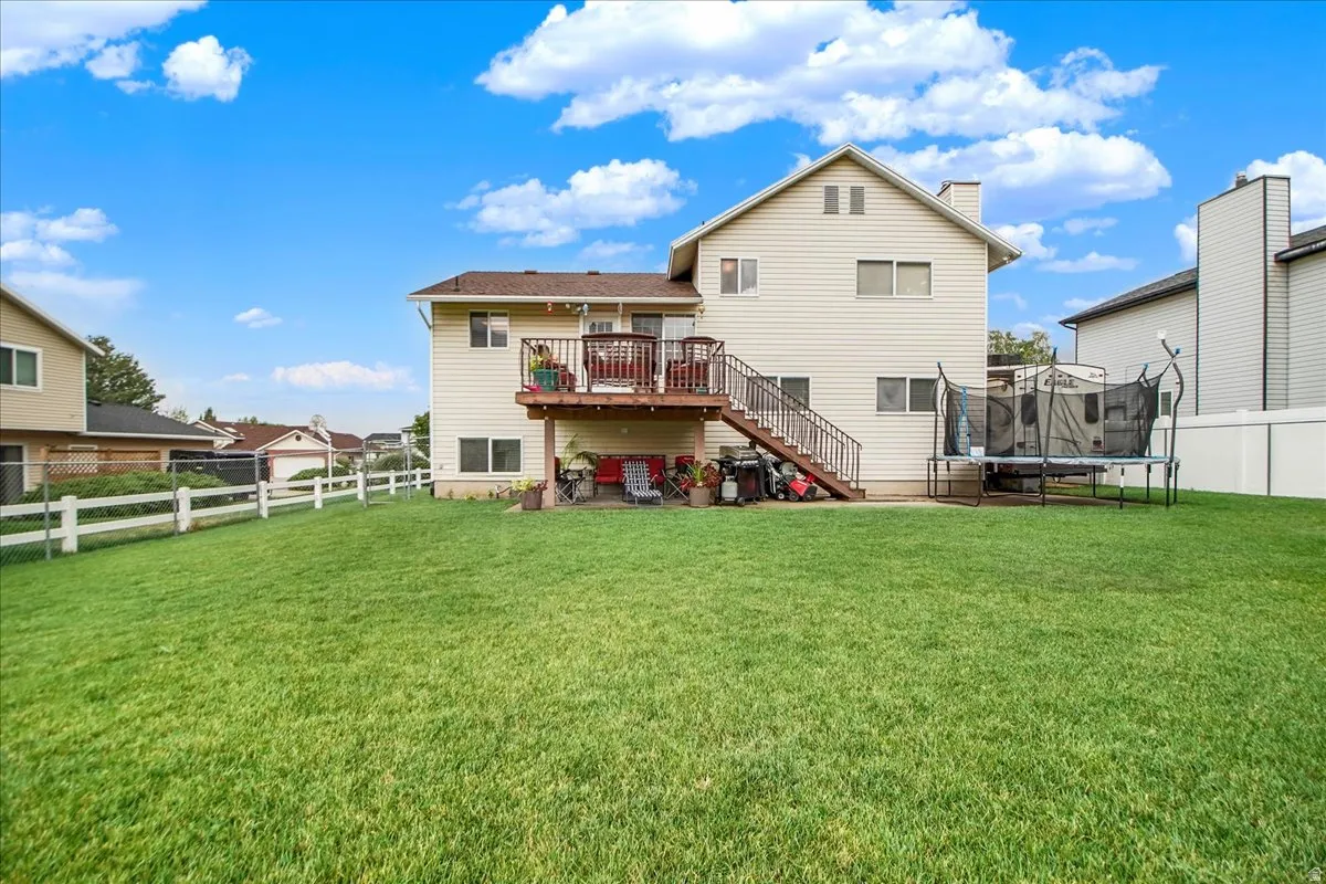 Expansive manicured lawn with mature landscaping, white fencing, and a two-story residence featuring a rear deck with metal railings