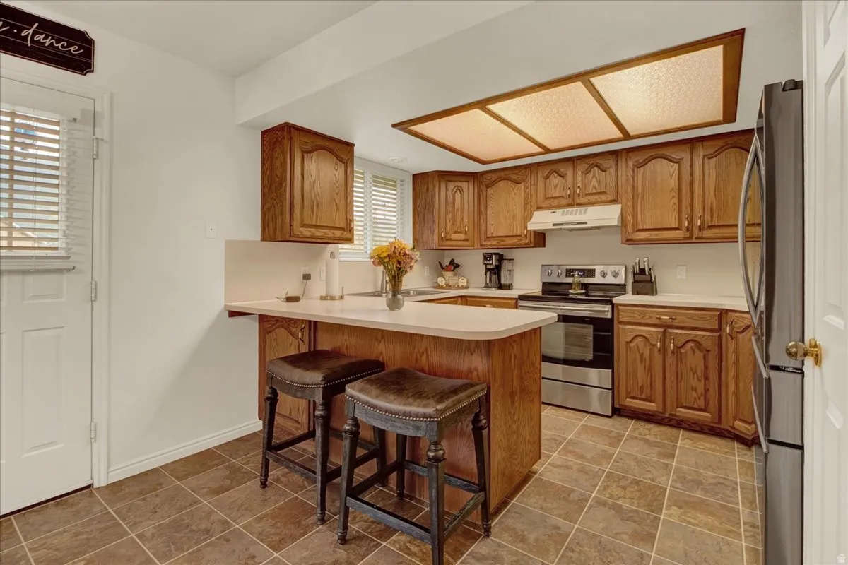 Warm wood cabinetry with detailed panel doors and crown molding, stainless steel appliances, and a tile-finish floor throughout