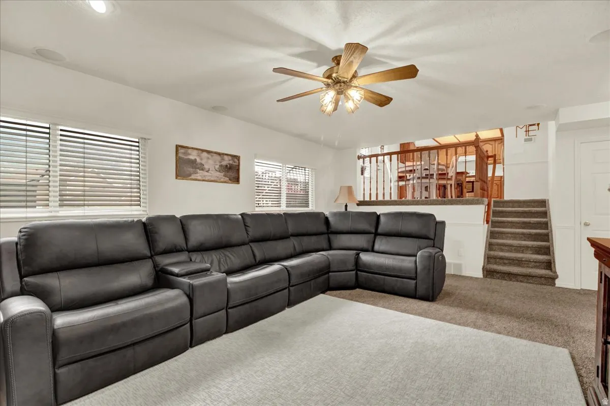 Spacious recreational room featuring a sectional layout with recessed lighting, ceiling fan with brass finish, neutral carpet flooring, and abundant natural light from multiple windows with plantation shutters