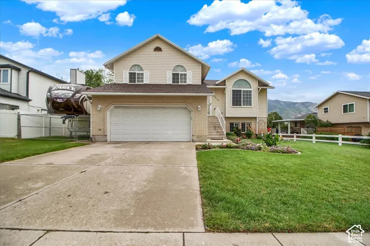 Two-story home featuring a tan exterior with arched windows, white two-car garage, concrete driveway, and manicured lawn with mature landscaping