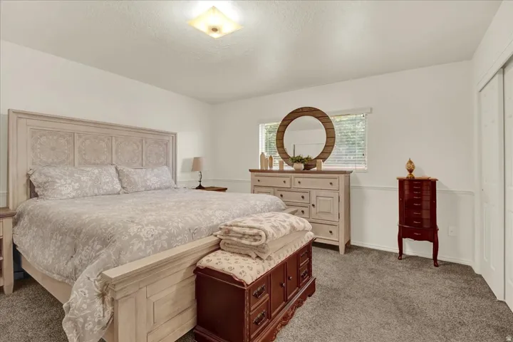Spacious primary bedroom featuring a decorative headboard with paneled detailing, neutral upholstered bedding, wood-finish dresser with multiple drawers, and abundant natural light from a large window