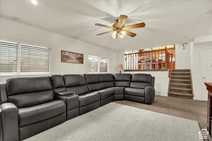 Spacious recreational room featuring a sectional layout with recessed lighting, ceiling fan with brass finish, neutral carpet flooring, and abundant natural light from multiple windows with plantation shutters