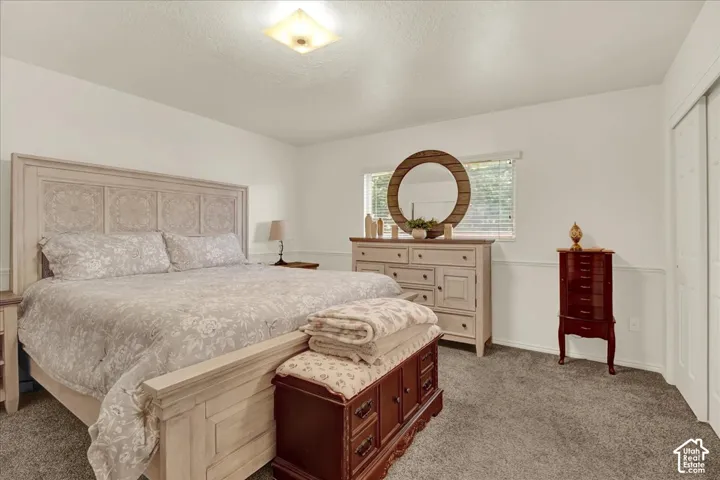 Spacious primary bedroom featuring a decorative headboard with paneled detailing, neutral upholstered bedding, wood-finish dresser with multiple drawers, and abundant natural light from a large window