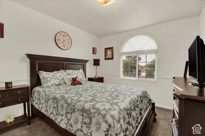 Spacious primary bedroom featuring dark wood furnishings, a decorative arched window with plantation shutters, neutral patterned bedding, carpeted flooring, and recessed ceiling lighting throughout the room