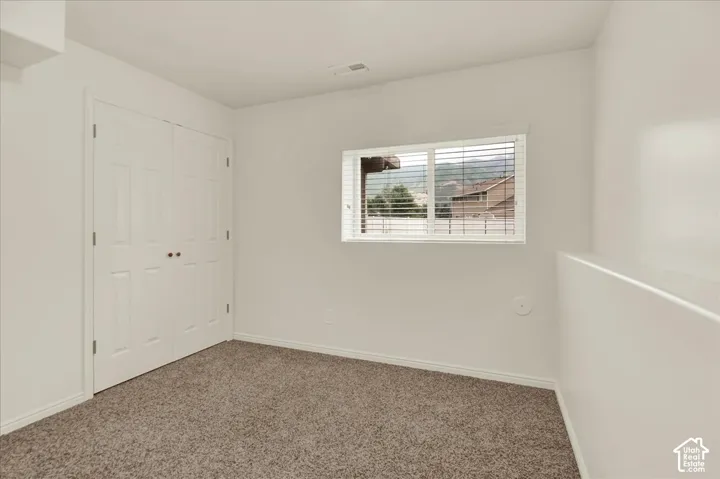 Bright secondary bedroom showcasing neutral wall finishes, carpet flooring, a double-door closet with white six-panel doors, and a horizontal window with exterior shutters allowing natural light