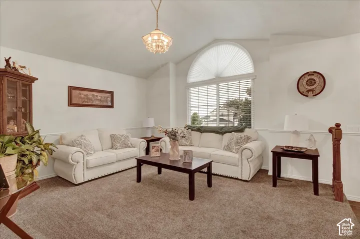 Vaulted ceiling with an ornate chandelier, large arched window, half-wall wainscoting, and carpeted flooring