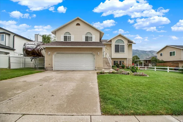 Two-story home featuring a tan exterior with arched windows, white two-car garage, concrete driveway, and manicured lawn with mature landscaping