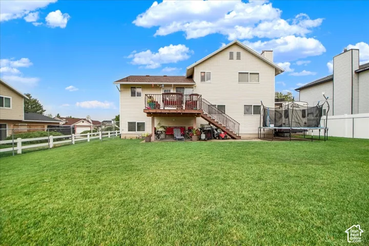 Expansive manicured lawn with mature landscaping, white fencing, and a two-story residence featuring a rear deck with metal railings