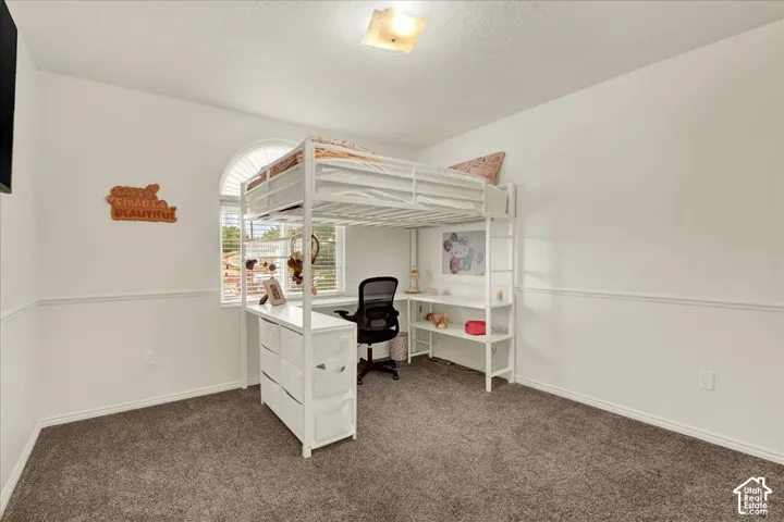 Versatile bedroom featuring a white metal loft bed with integrated desk and storage shelving, gray carpeting, recessed ceiling lighting, and ample wall space for personalization