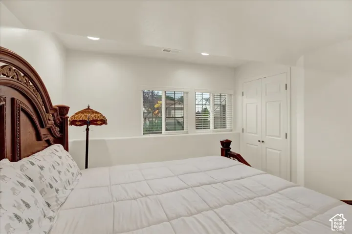 Spacious primary bedroom featuring elegant wood-finish headboard with carved detailing, recessed ceiling lighting, plantation shutters, and dual closet doors