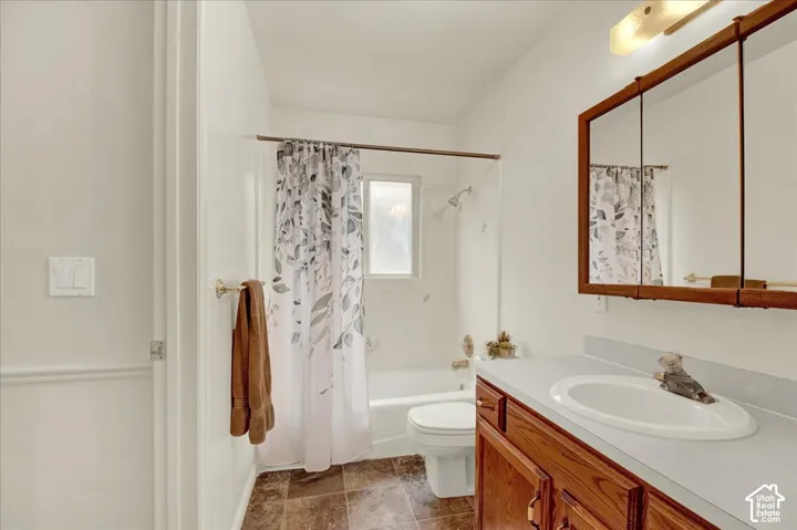 Full bathroom featuring a wood-finish vanity with dual white oval sinks, ceramic tile flooring, white subway tile walls, a toilet, and a framed mirror with wood trim