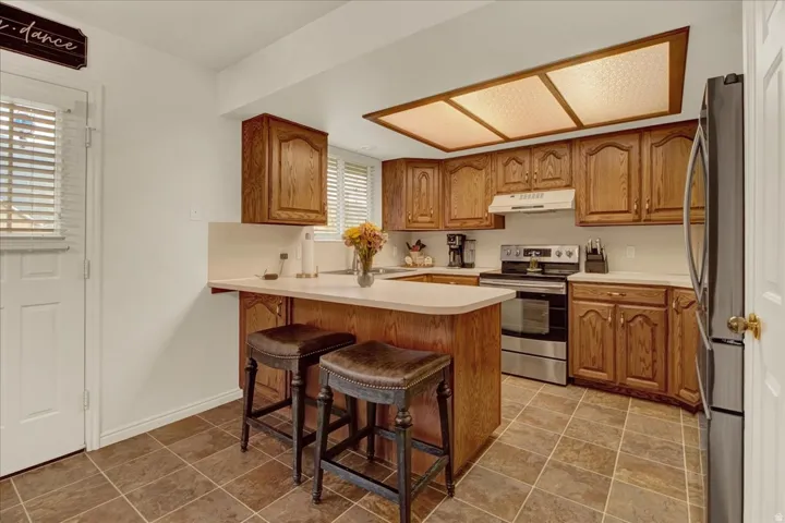 Warm wood cabinetry with detailed panel doors and crown molding, stainless steel appliances, and a tile-finish floor throughout