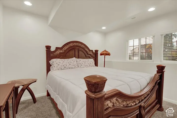 Elegant primary bedroom showcasing ornate wood-carved bed frame with upholstered headboard, recessed ceiling lighting, plantation shutters, and neutral wall finishes