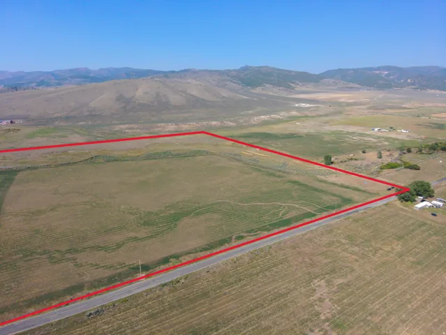 Expansive land parcel featuring open fields, a paved road frontage, and distant mountains