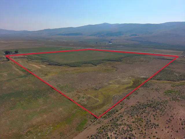 Expansive rural acreage featuring diverse terrain, a cultivated field, and distant mountain backdrops
