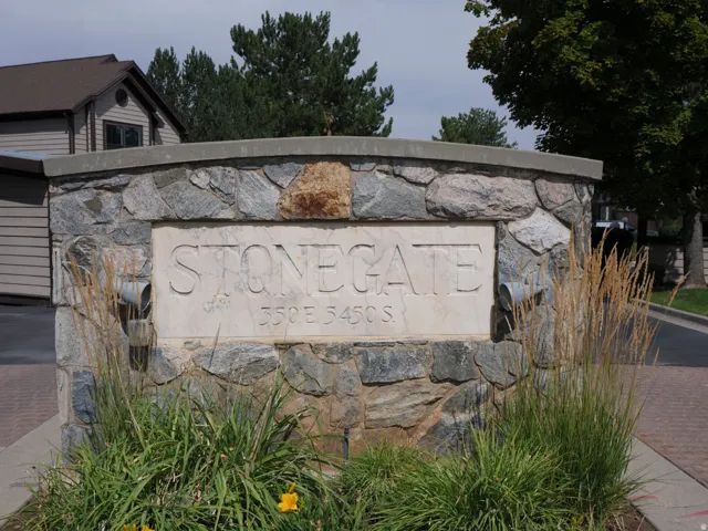 Stonegate community entrance featuring a curved stone monument with carved lettering, complemented by mature landscaping and brick paver hardscaping