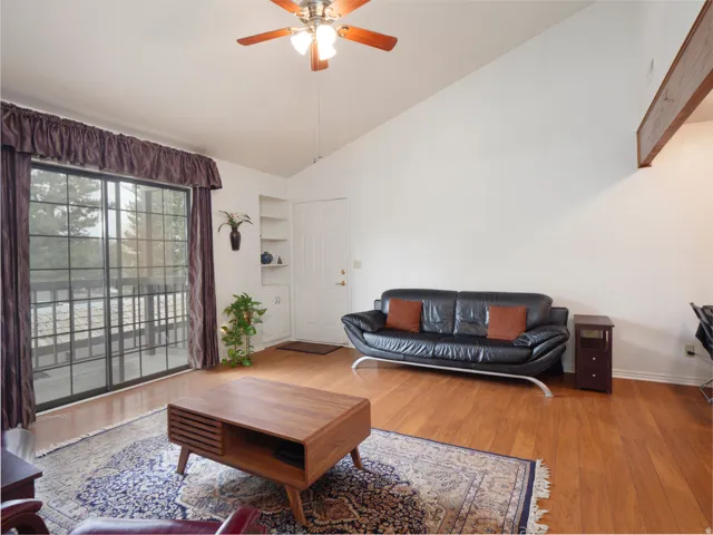 Vaulted ceiling, wood-finish flooring, built-in shelving, ceiling fan, and sliding glass door