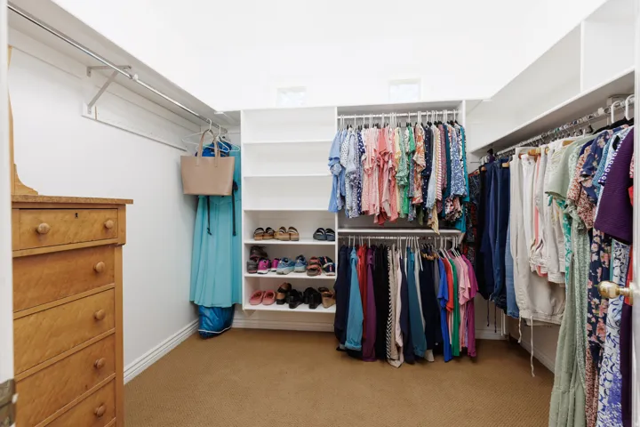 Spacious walk-in closet featuring extensive built-in shelving and hanging rods, wood-finish flooring, and abundant natural light from recessed ceiling fixtures