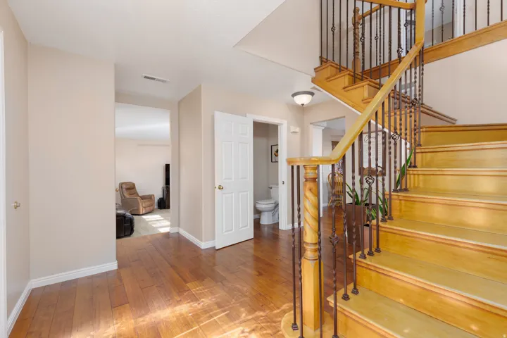 Hardwood flooring throughout the entry, a wooden staircase with wrought iron balusters, and a white six-panel door