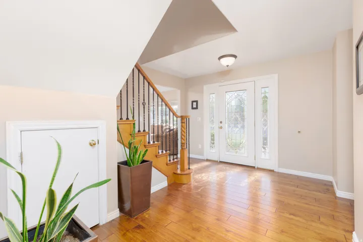 Hardwood-finish flooring, staircase with wood handrail and wrought iron spindles, white door with decorative glass panels, transom window, and flush mount ceiling light