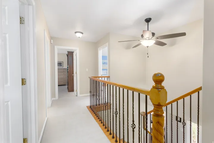 Carpeted hallway with a wood and wrought iron staircase railing, semi-flush mount lighting, and a ceiling fan with integrated lighting