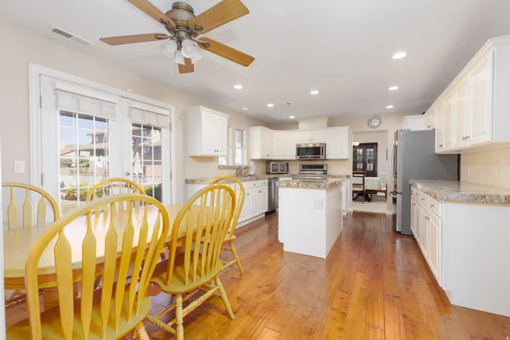 Bright, open-concept kitchen featuring white cabinetry, stainless steel appliances, granite countertops, a central island with prep space, and hardwood flooring throughout