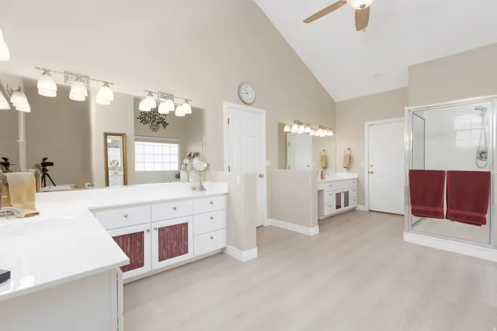 Vaulted ceiling, ceiling fan, wood-finish flooring, dual vanity areas, and a glass-enclosed shower