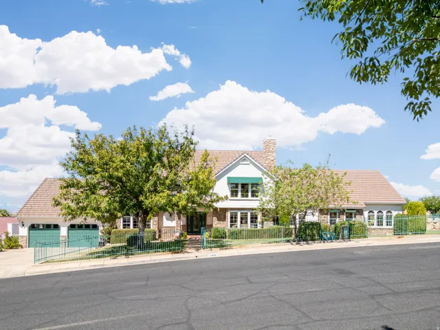 Charming brick Colonial featuring a welcoming front entrance with arched doorway, dual garage doors with green accents, and mature landscaping including established trees