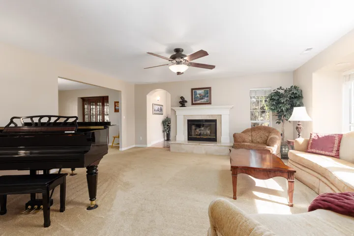 Recessed fireplace with a light-toned mantle, archway, ceiling fan, and carpeted flooring