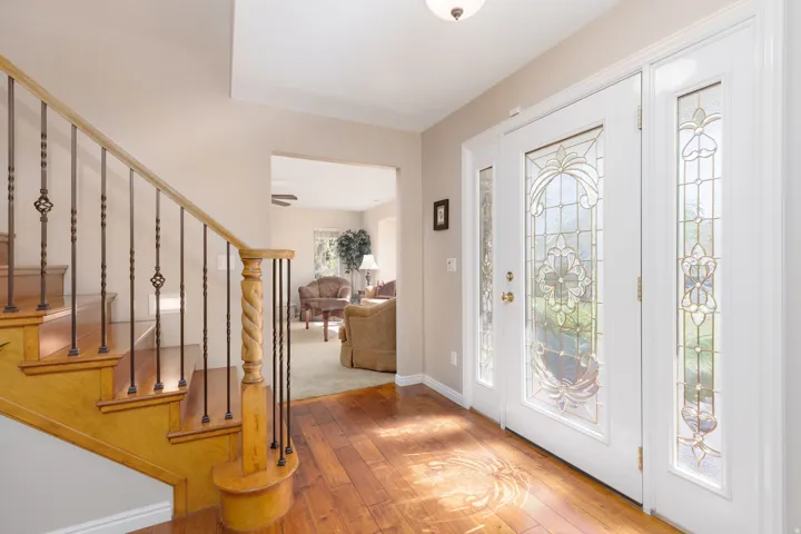 Welcoming foyer showcasing warm wood-finish flooring, a curved wooden staircase with wrought iron balusters, and French doors with decorative glass panels flooding the space with natural light