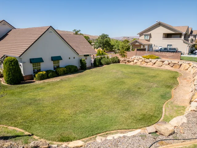 Expansive backyard featuring a manicured lawn, stone retaining walls, and mature landscaping