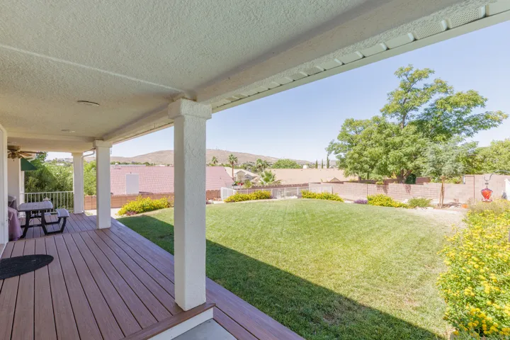 Covered patio with composite decking, white columns, and ceiling fan overlooking a spacious lawn and distant hills