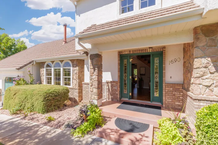 Welcoming entry featuring a stone and brick exterior with dark green paneled doors, arched transom windows, and mature landscaping framing the approach