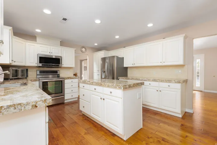 Kitchen featuring a center island, wood-finish flooring, white cabinetry, stainless steel appliances, and stone countertops