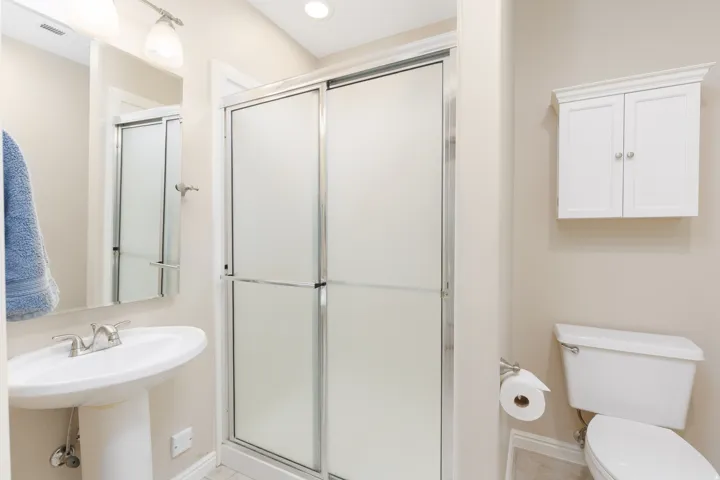 Pedestal sink with a chrome faucet, mirrored vanity, sliding glass shower enclosure, recessed lighting, and wall-mounted cabinetry