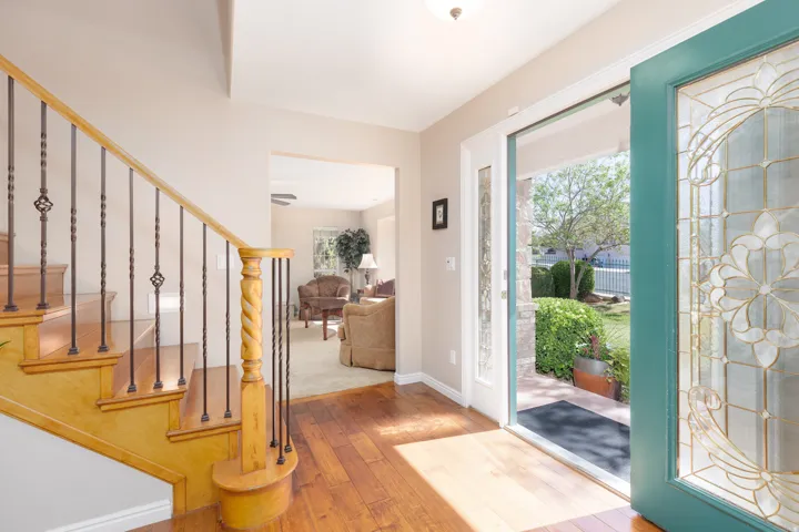 Welcoming foyer showcasing warm wood-finish flooring, a natural wood staircase with black metal railings, and abundant natural light streaming through a teal-framed glass door