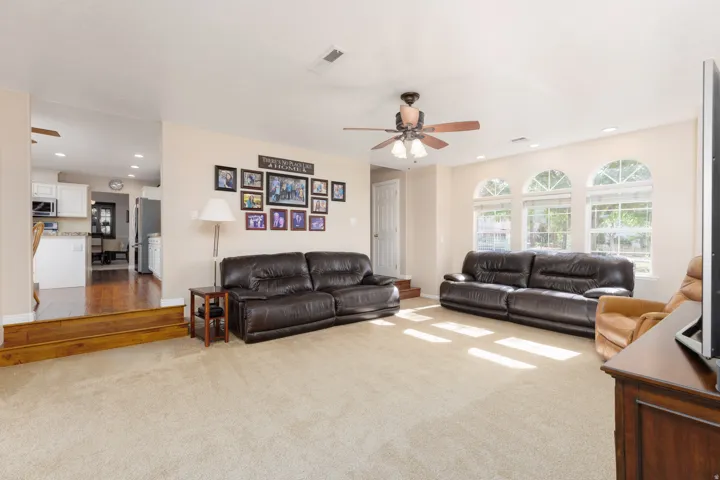 Recessed lighting illuminates this expansive space featuring arched windows, a ceiling fan, and carpet flooring