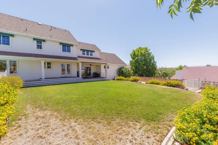 Expansive green lawn with established shrubbery, covered patio, and multi-level deck