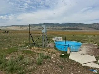Expansive open terrain with natural vegetation, featuring a blue water trough and a utility structure on a concrete pad