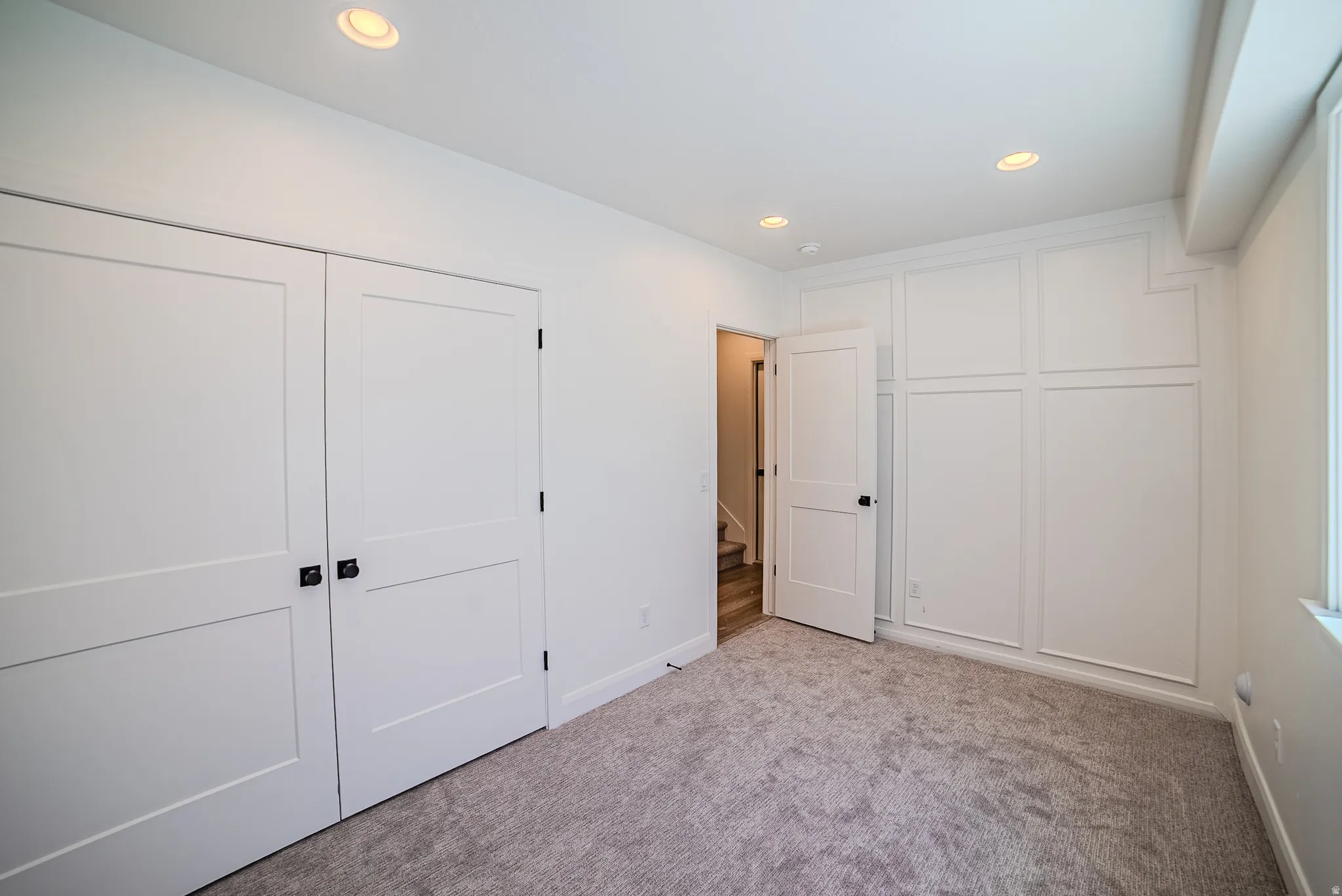 Recessed lighting illuminates the room, featuring a carpeted floor, white walls, and a window providing natural light