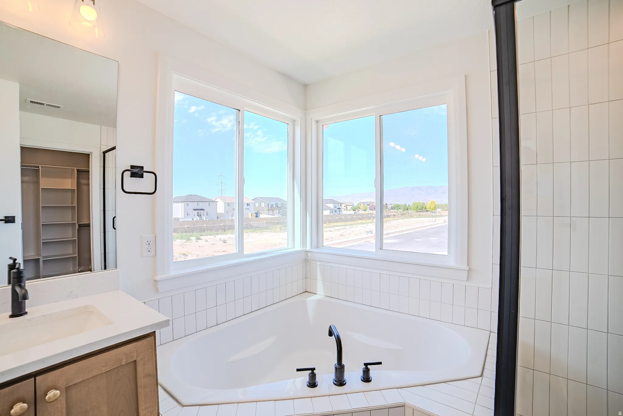 Corner soaking tub with matte black fixtures, dual windows, full-height mirror, and a built-in closet system