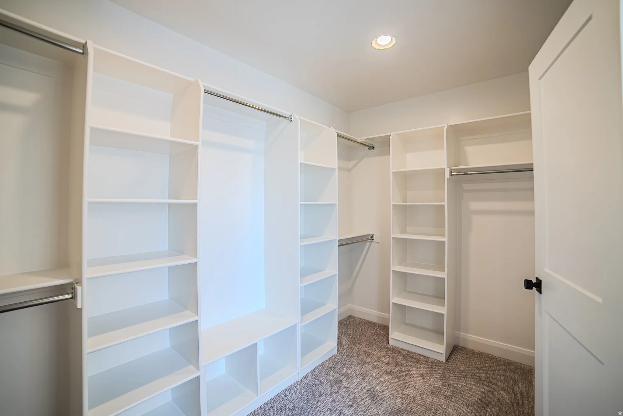 Built-in closet organization system featuring multiple shelving units, hanging rods, recessed lighting, and soft carpet flooring