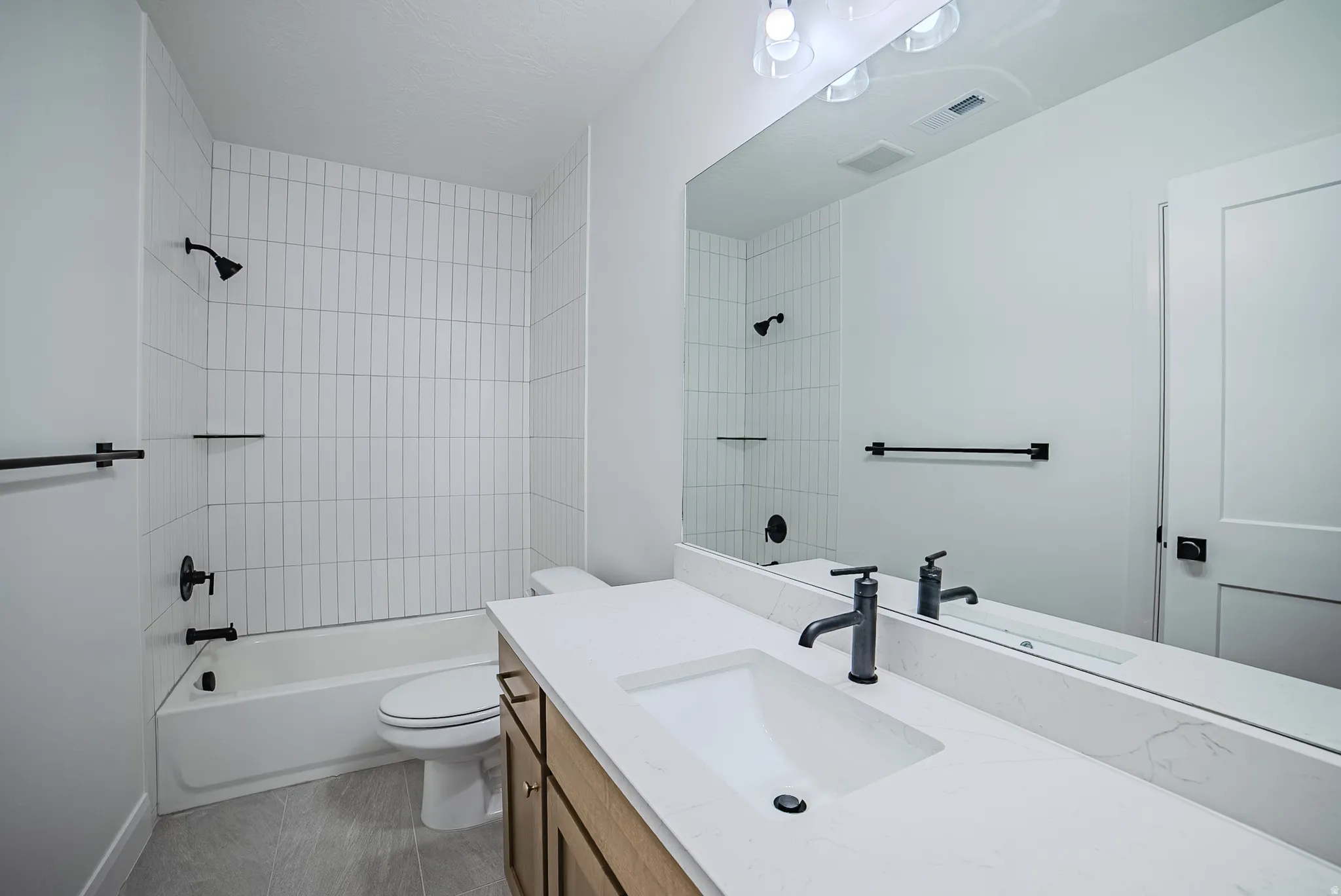 Bathroom featuring a tub/shower combination with vertical subway tile surround, single vanity with integrated sink, matte black fixtures, and a frameless mirror