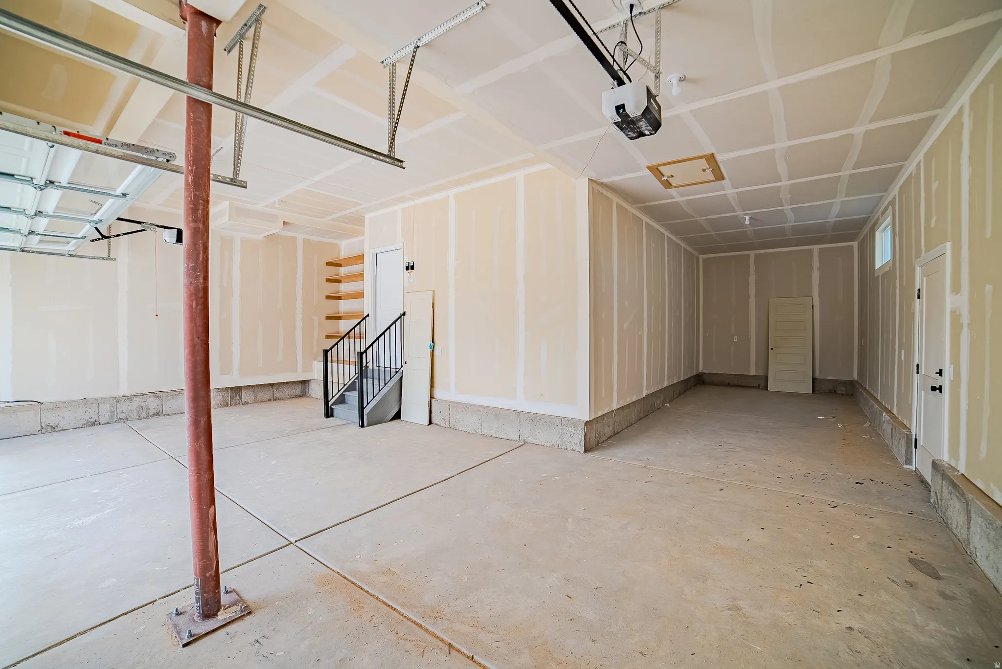 Spacious garage with concrete flooring, built-in wooden shelving, and a black wrought iron staircase