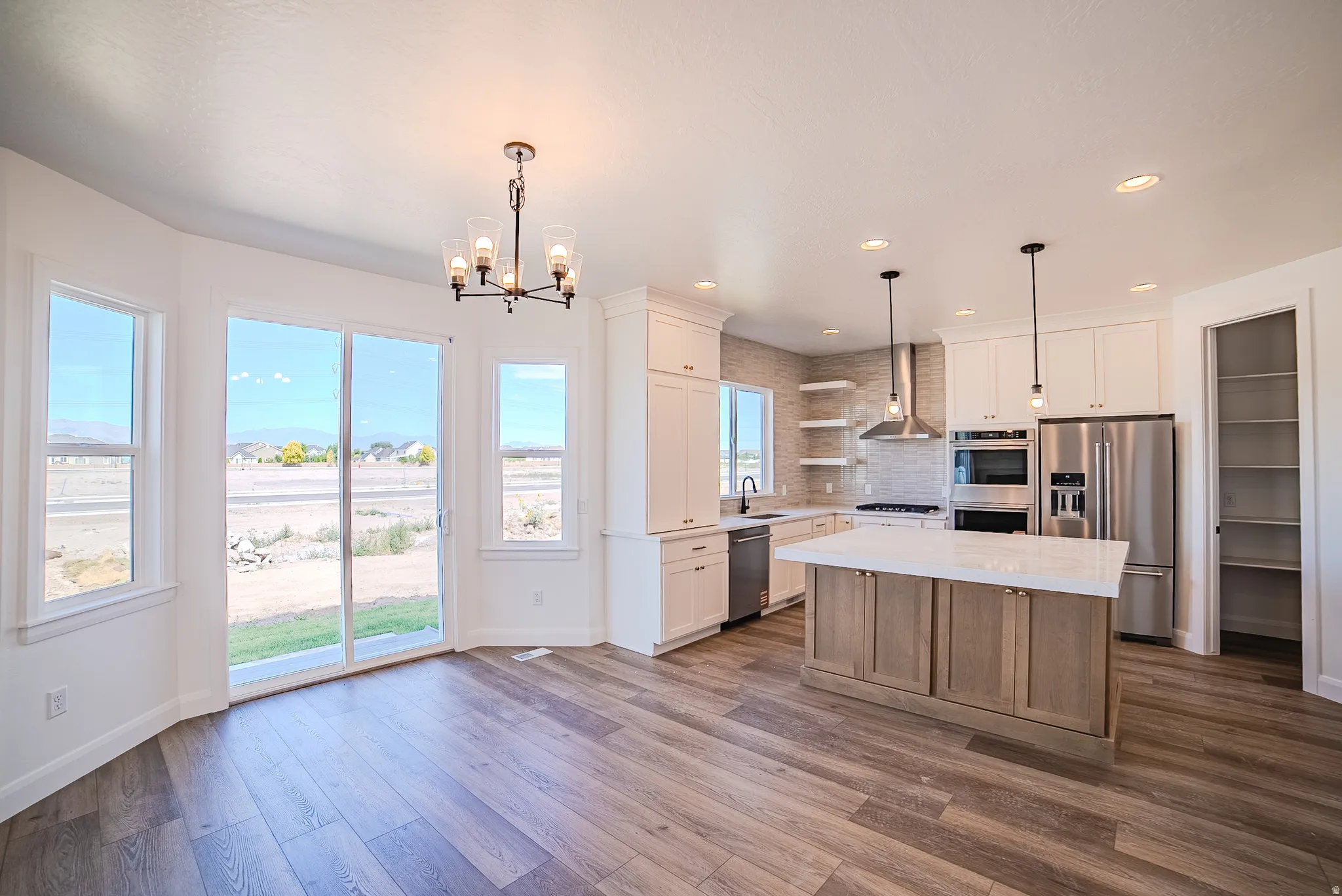 Wood-finish flooring, white cabinetry, stainless steel appliances, and a central kitchen island with a light-colored countertop