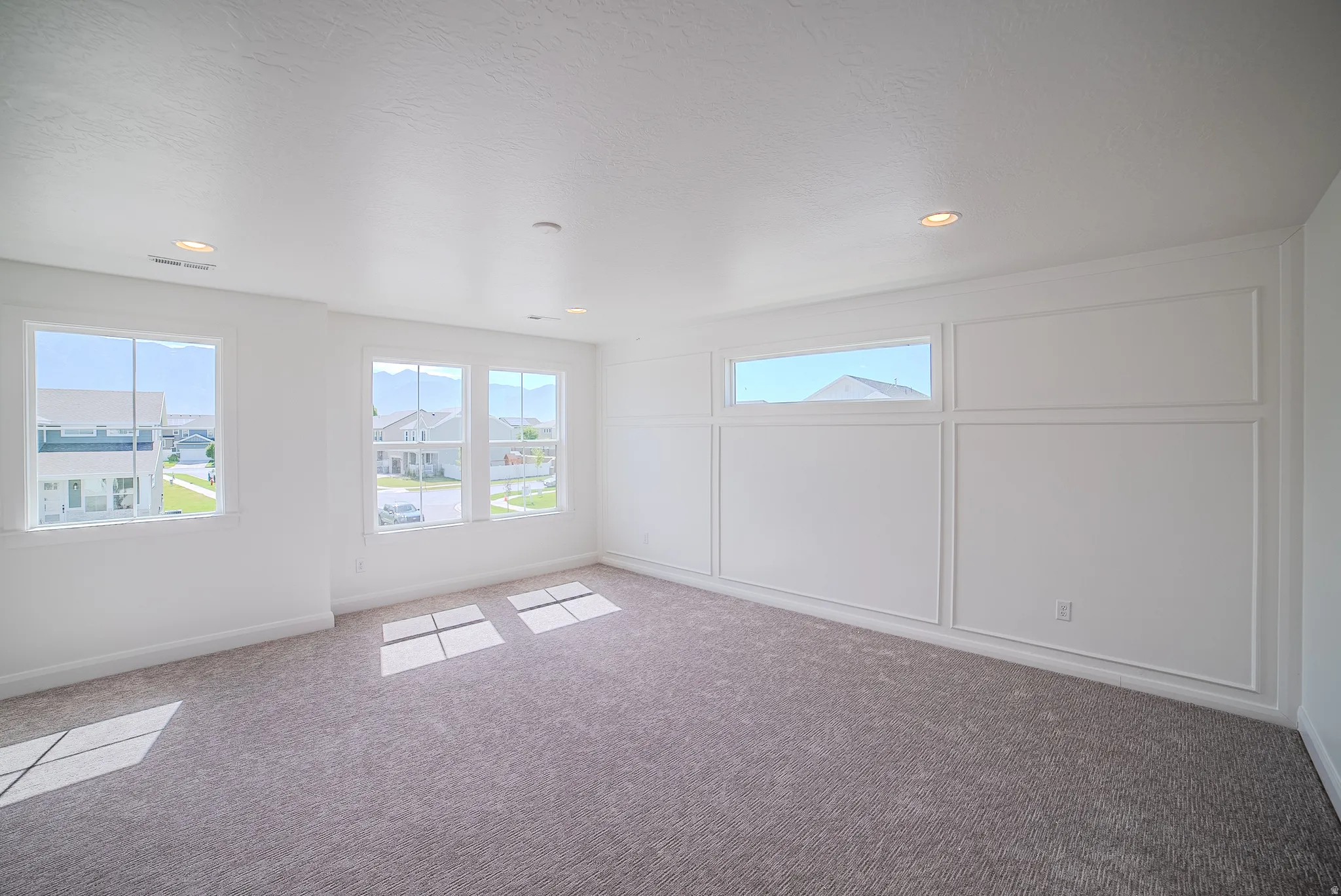 Neutral-toned carpeting, recessed ceiling lighting, multiple windows, and decorative wall paneling