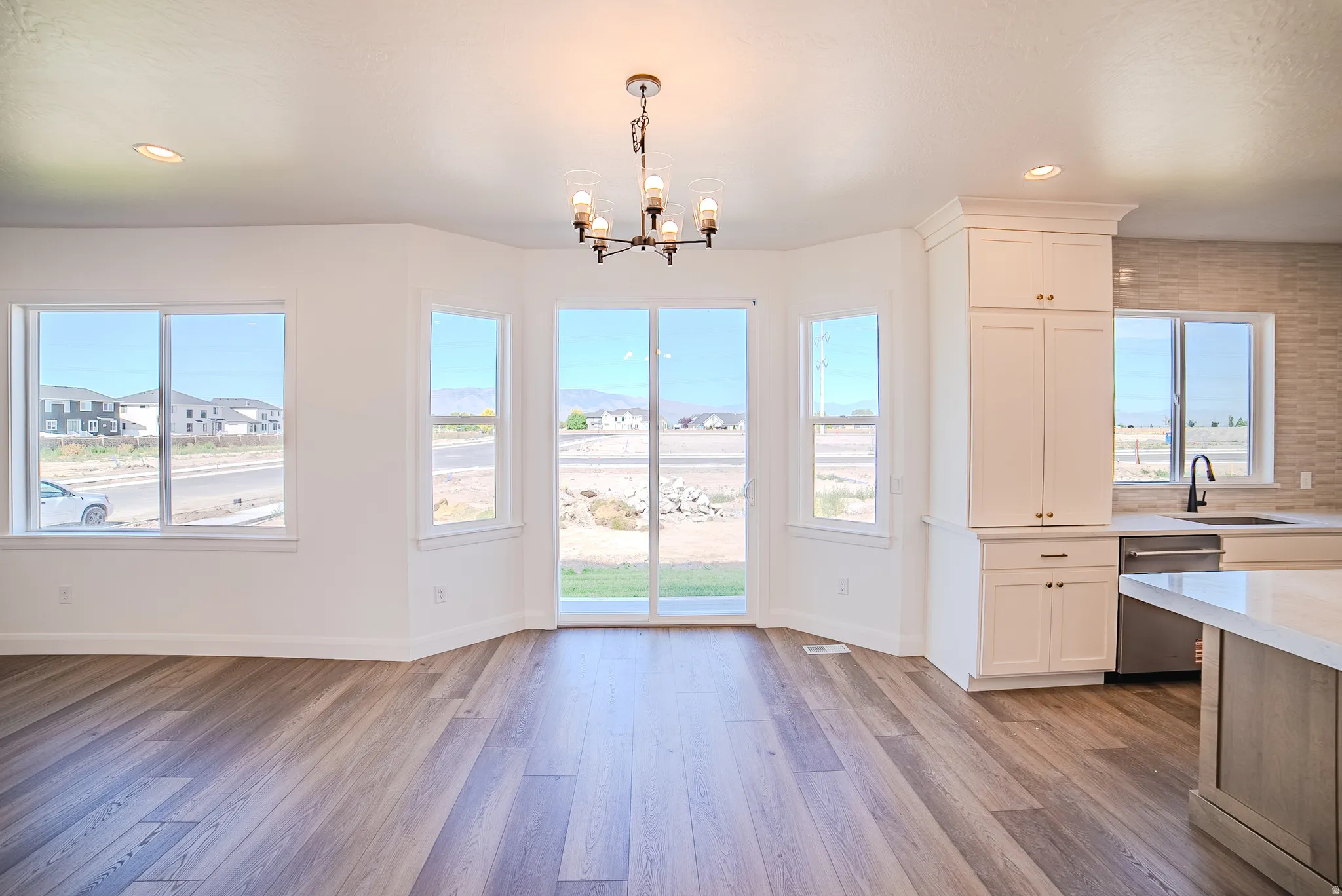 Wood-finish flooring throughout, white cabinetry with crown molding, recessed lighting, and a modern chandelier