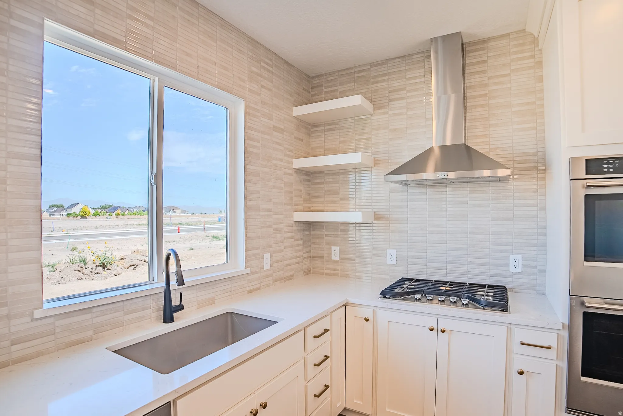 Modern kitchen featuring white cabinetry with brass hardware, a stainless steel range hood, gas cooktop, and integrated wall-mounted double ovens